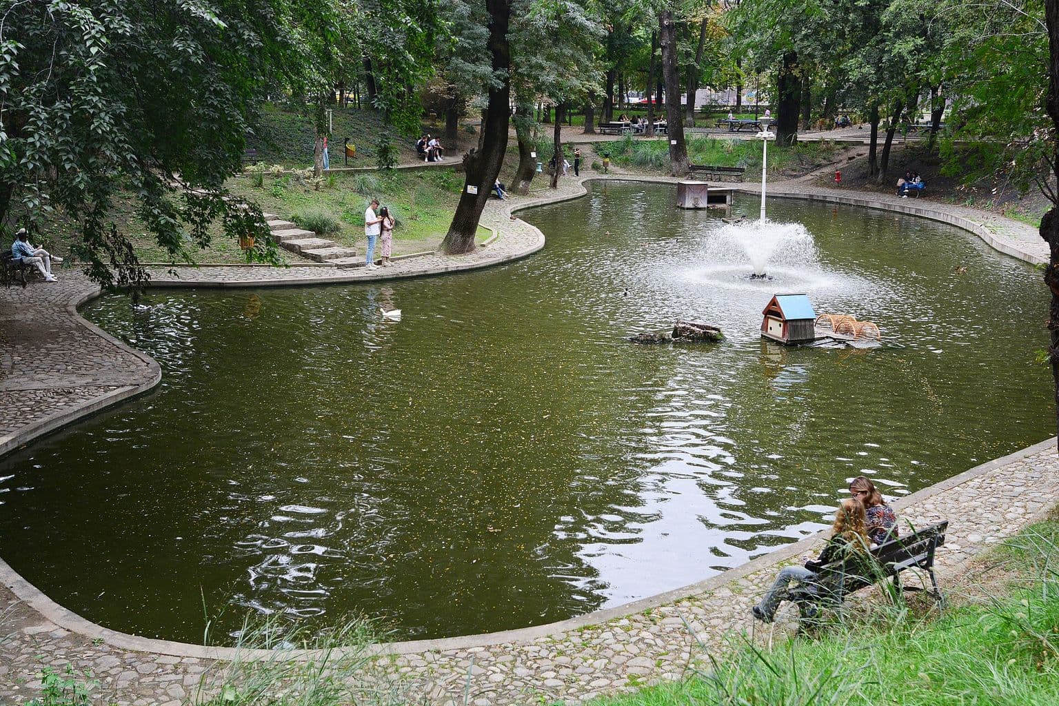 Lacul mic din Parcul Kiseleff, cu o fântână arteziană și o căsuță pentru rațe, între alei de piatră și copaci înalți