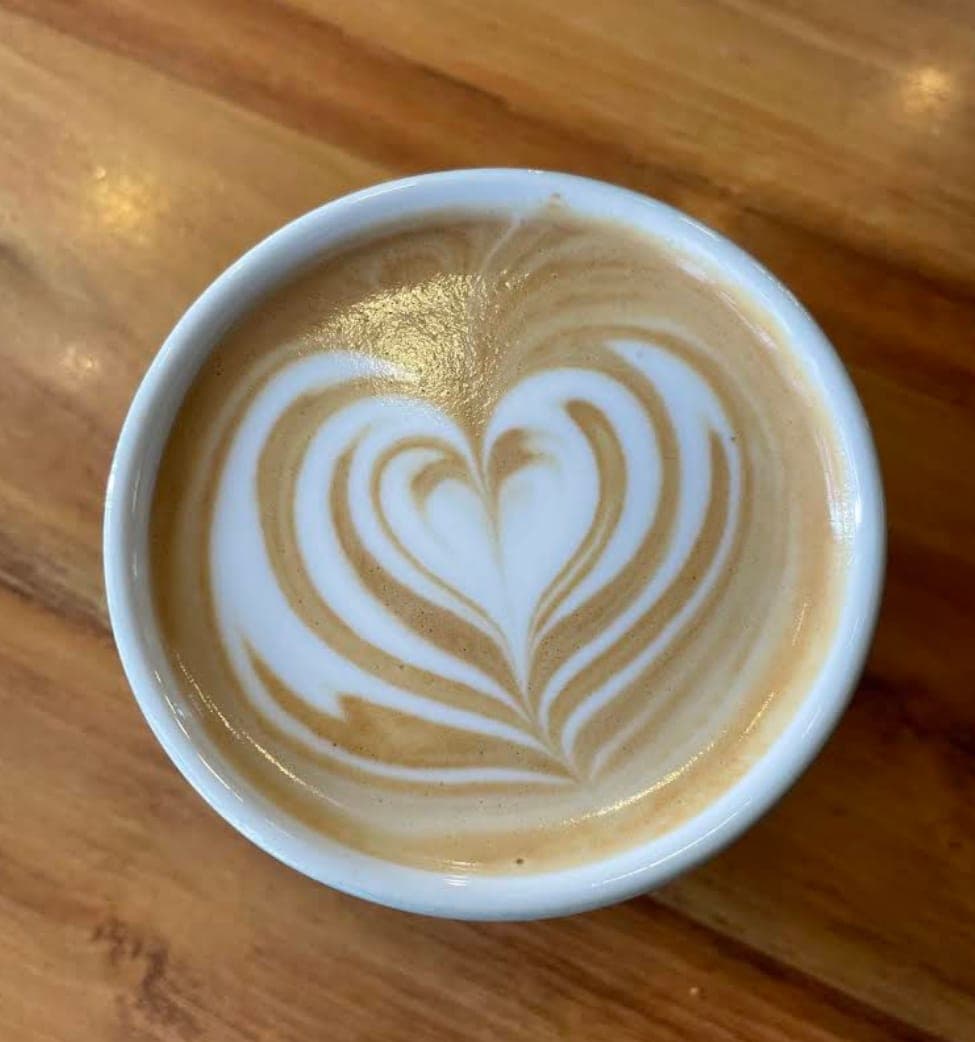 Café au lait avec un latte art en forme de cœur, dans une tasse blanche, vu d’en haut sur une table en bois verni