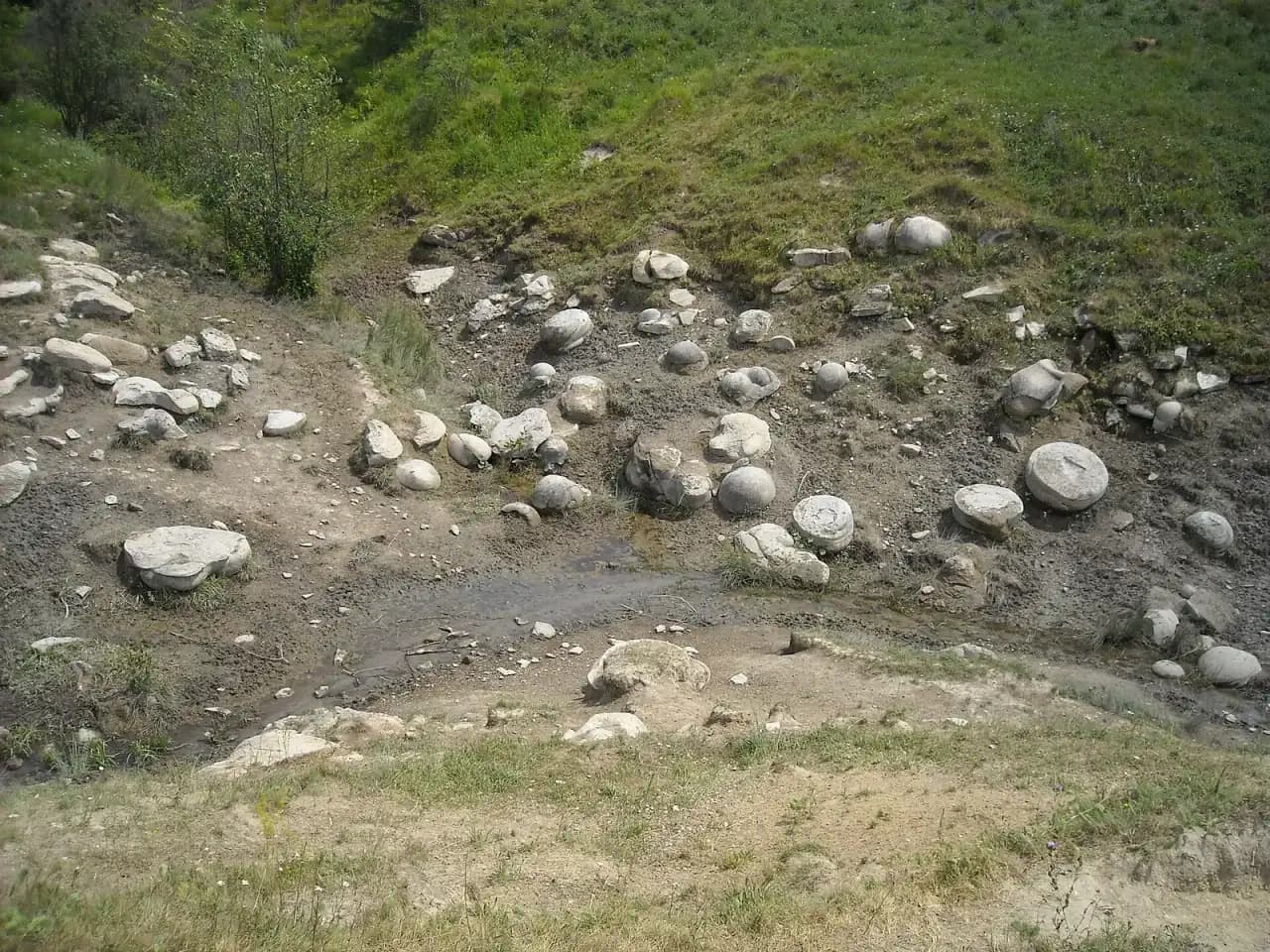Trovanți rotunzi și cenușii, ca niște ouă mari de piatră, împrăștiați într-o râpă cu un firicel de apă, sub o pantă cu iarbă, lângă Feleacu